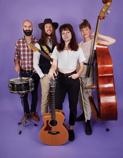 Portrait du groupe "Karoline and the Free Folks" en studio, sur fond violet, avec des instruments de musique.