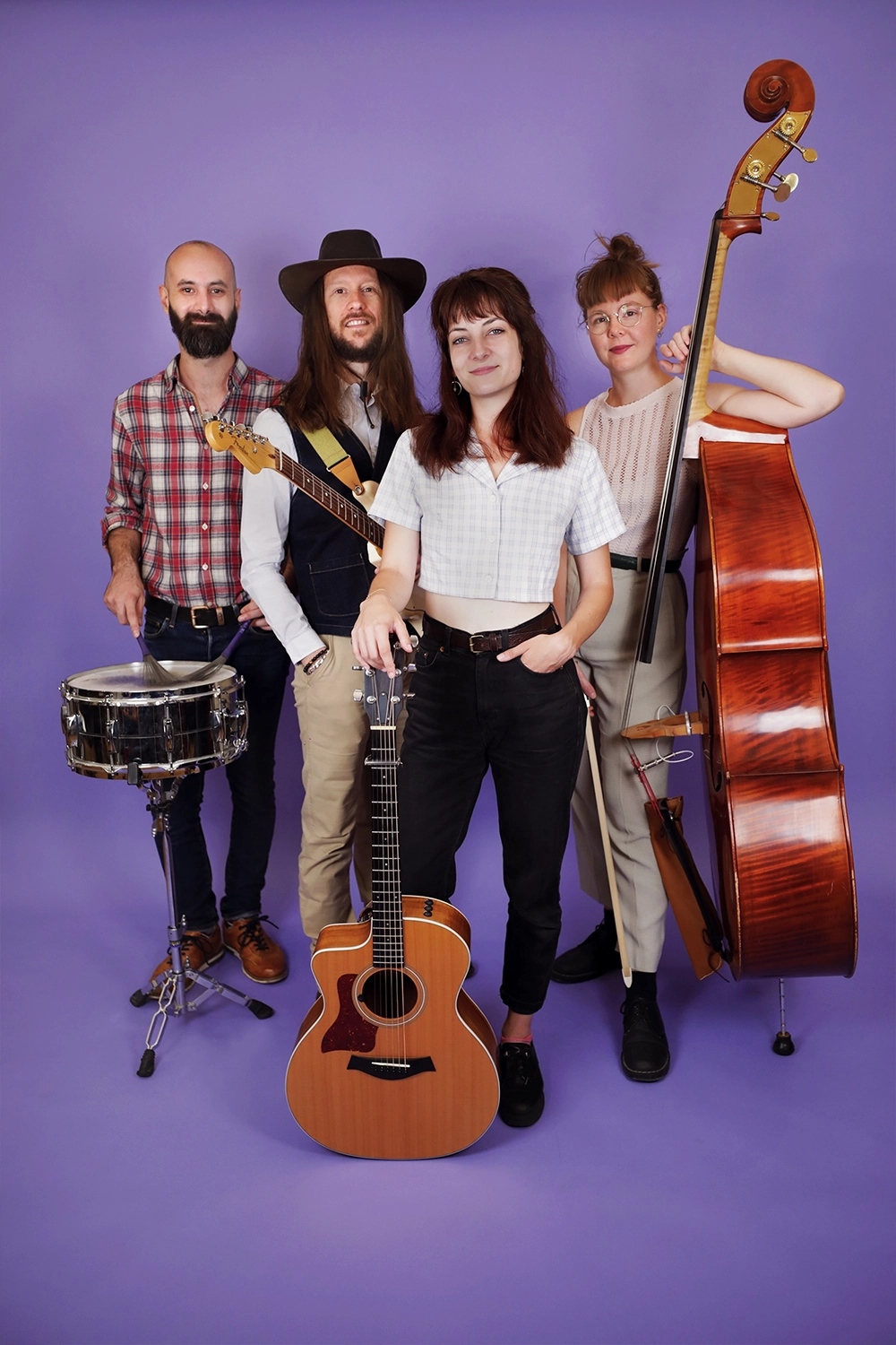 Portrait du groupe "Karoline and the Free Folks" en studio, sur fond violet, avec des instruments de musique.
