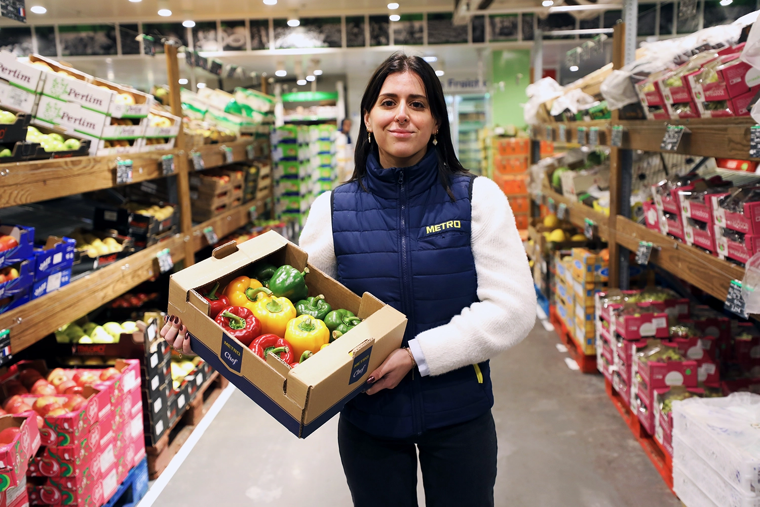 Alternante METRO en rayon fruits et légumes avec un carton de poivrons colorés.
