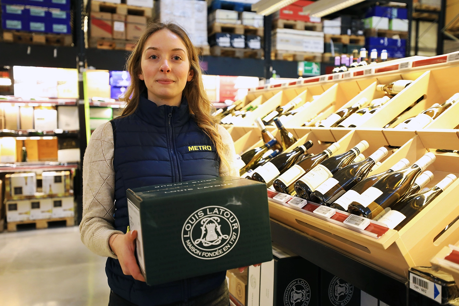 Alternante METRO présentant une caisse de vins dans le rayon spiritueux.