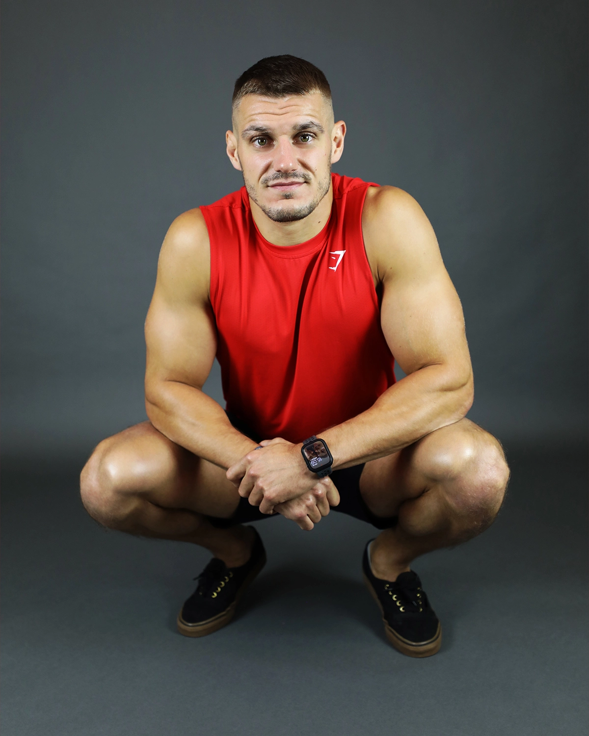 Portrait en studio d’un coach sportif en débardeur gris et short rouge.