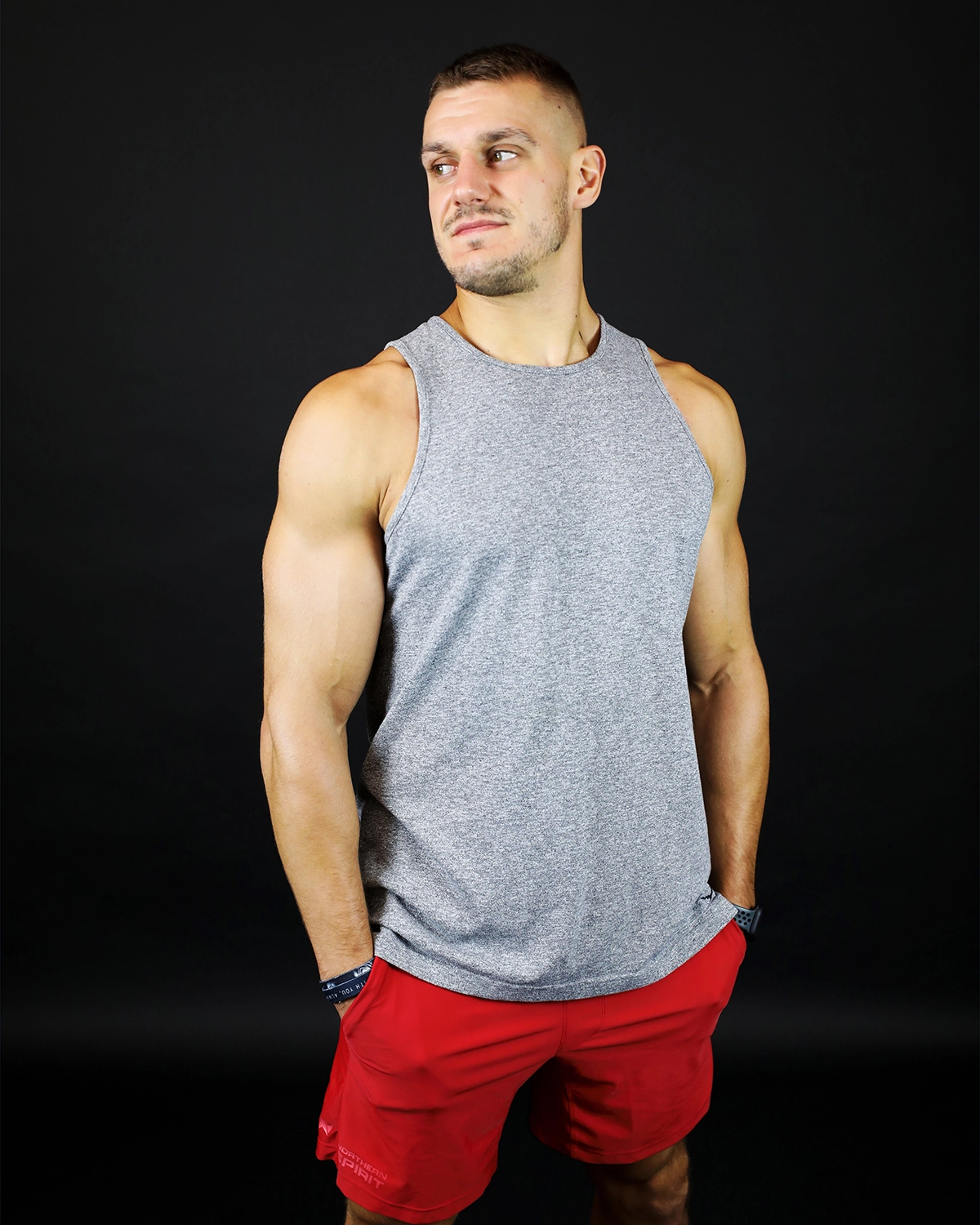 Coach sportif en short rouge et débardeur gris, posant dans un studio photo.