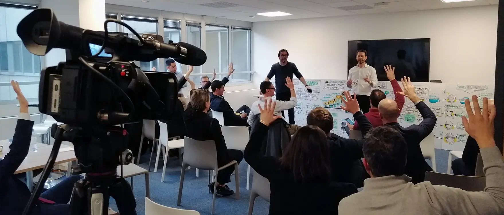 Captation vidéo d'un atelier inter-entreprise avec participants levant la main pour répondre, animée par deux intervenants. Contexte professionnel dans un espace lumineux et moderne