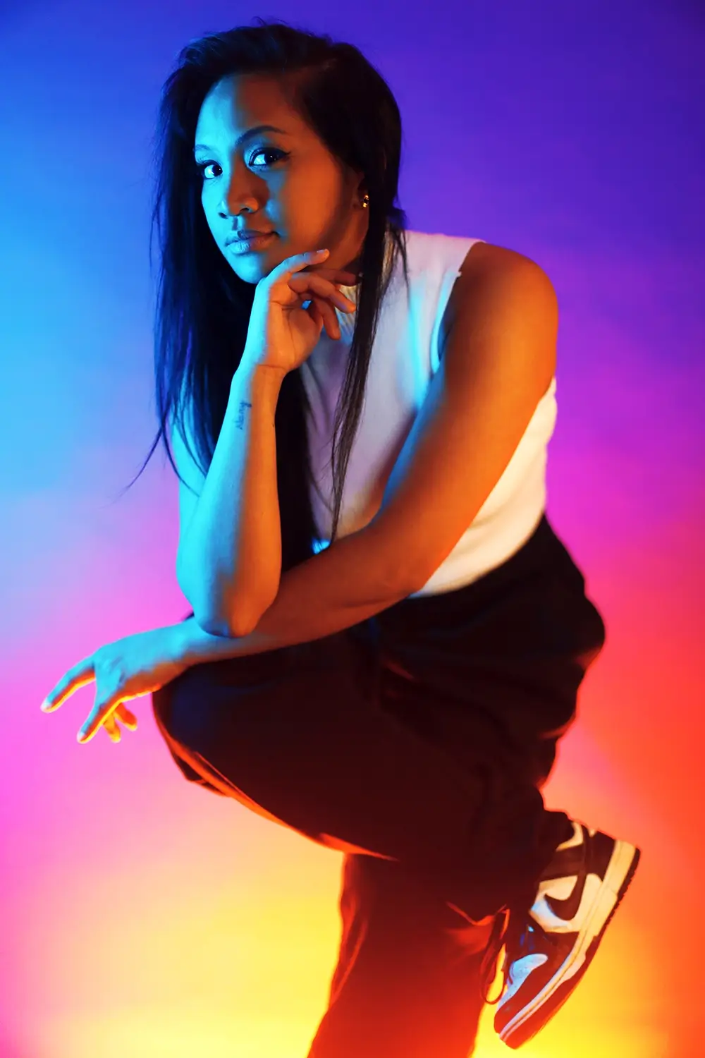 Portrait artistique en couleurs néon Portrait artistique d’une femme accroupie, éclairée par des lumières bleues, violettes et orangées.