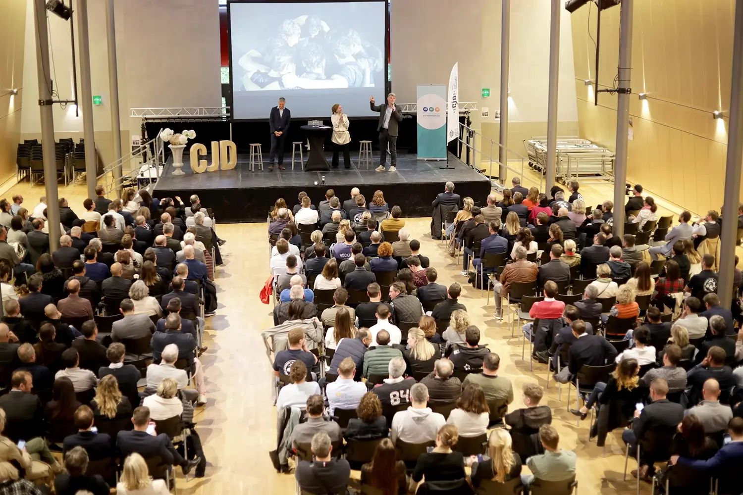 Conférence du CJD – vue d’ensemble Conférence du CJD vue depuis la salle, avec les intervenants sur scène et le public