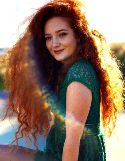 Femme rousse en robe verte photographiée en extérieur, éclairée en contre-jour avec un reflet arc-en-ciel.