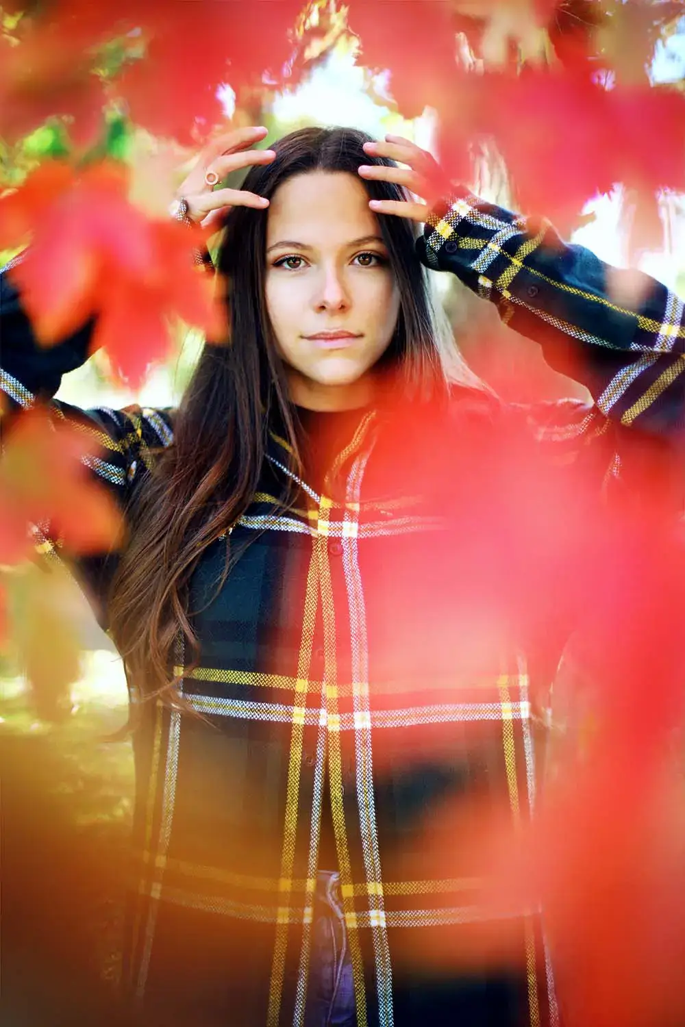 Portrait en extérieur parmi les feuilles rouges Femme brune en chemise à carreaux posant derrière des feuilles rouges floues en extérieur.