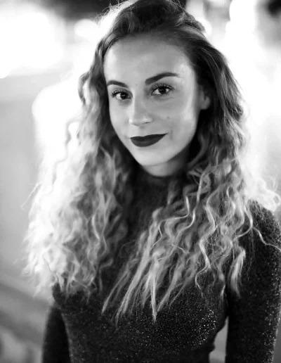 Portrait en noir et blanc d’une femme aux cheveux bouclés regardant l’objectif.