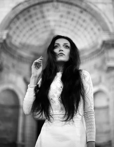 Femme en robe blanche photographiée en noir et blanc devant une architecture monumentale.