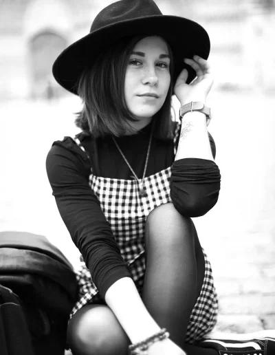 Femme portant un chapeau noir, assise en extérieur, photographiée en noir et blanc.