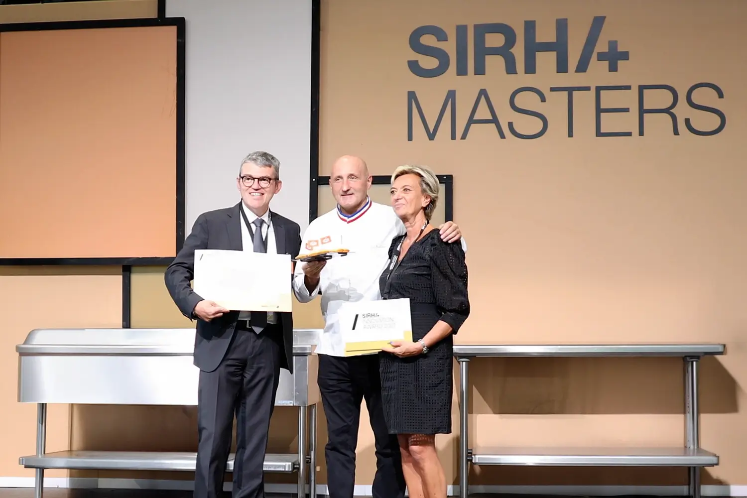 SIRHA+ Masters – remise de prix Trois personnes, dont un MOF sur scène lors d’une remise de prix au SIRHA+ Masters à Lyon
