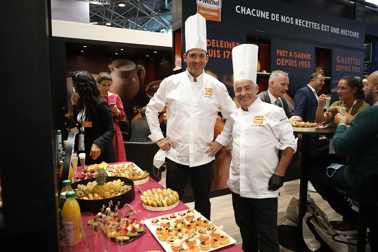 Salon SIRHA – Stand St Michel Biscuits Deux chefs sur un stand de St Michel Biscuits au SIRHA à Lyon, devant un buffet et des visiteurs