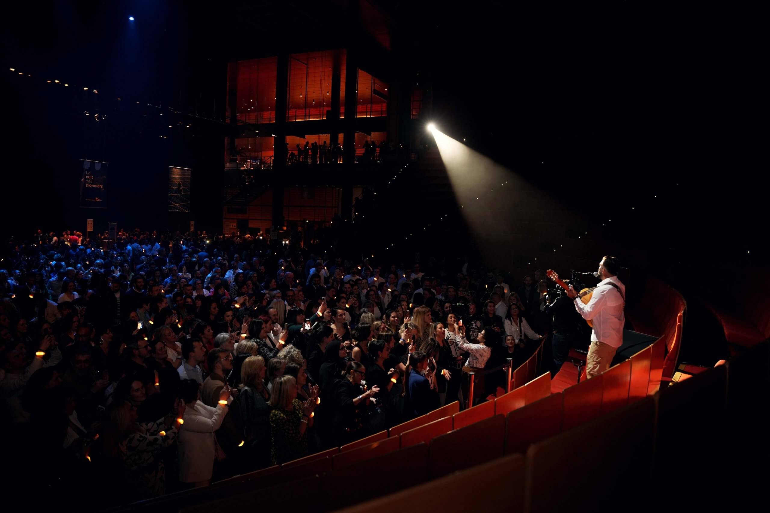 Kendji Girac face au public de la salle 3000 à Lyon Guitariste éclairé par un projecteur, vu de dos face au public dans une salle de spectacle.