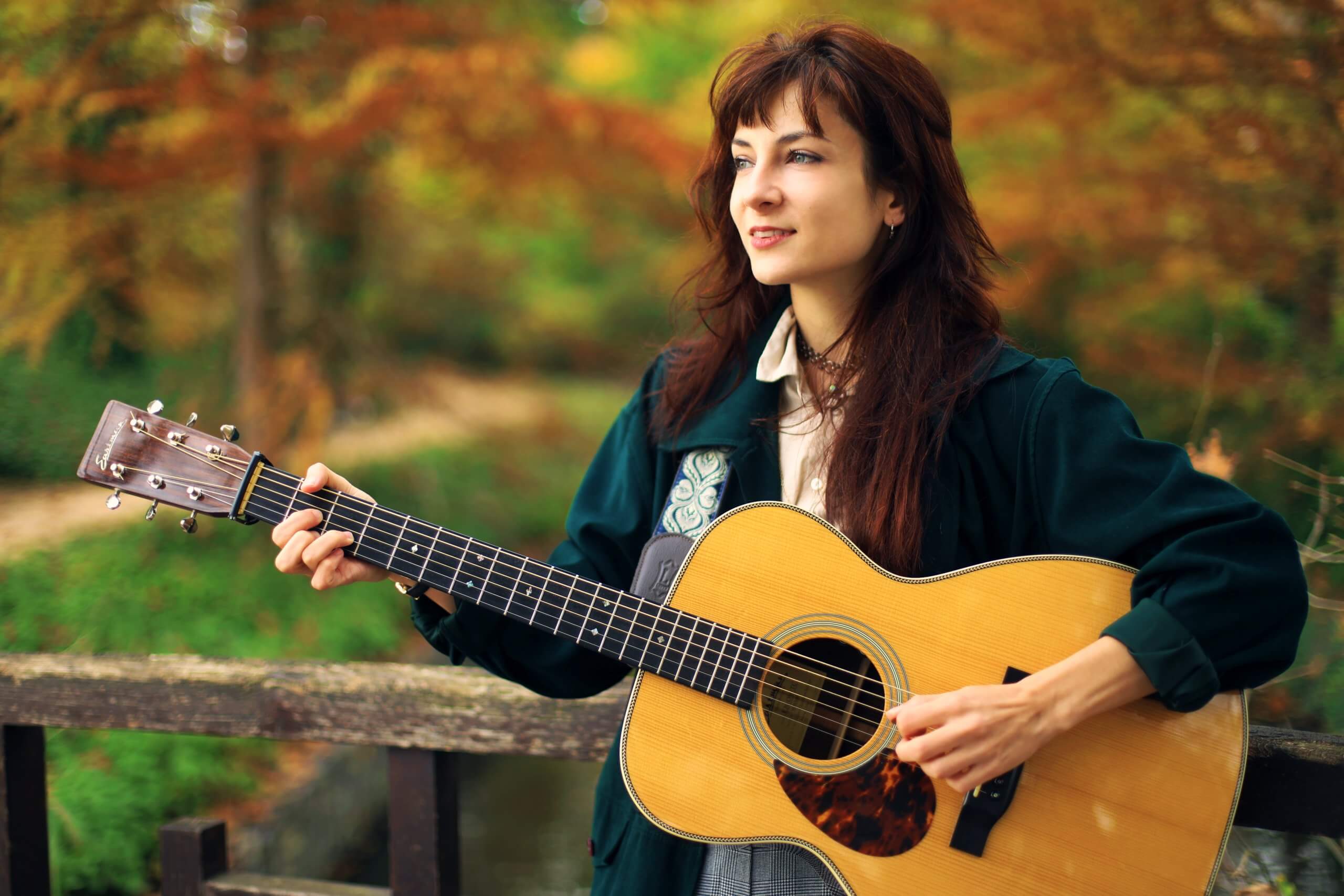 Karoline & the Free Folks - portrait à la guitare en extérieur Karoline pose avec une guitare acoustique devant un paysage aux couleurs automnales.