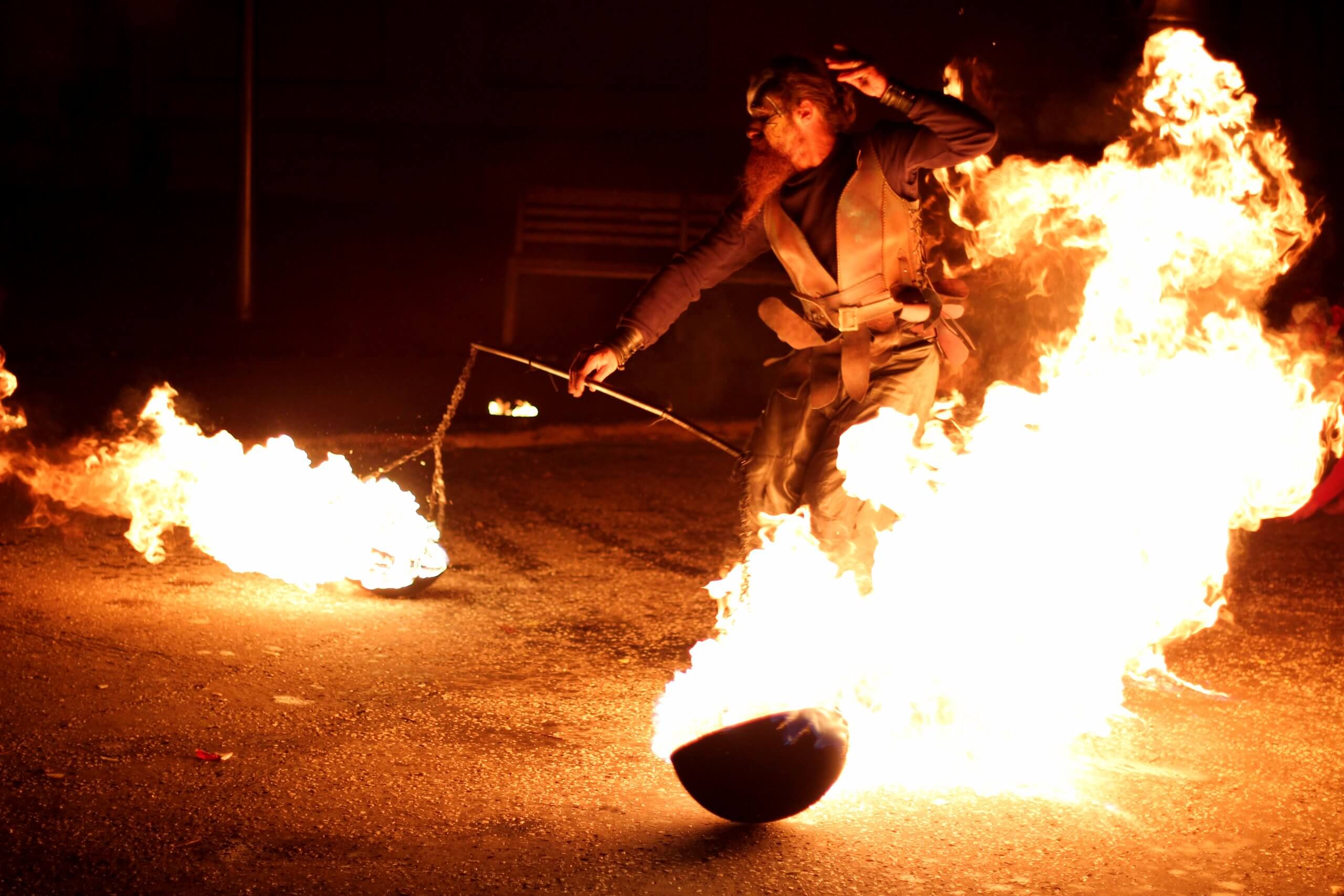 Spectacle de rue - artiste et manipulation de feu Un artiste manipule des accessoires enflammés dans la rue, de nuit, entouré de grandes flammes.
