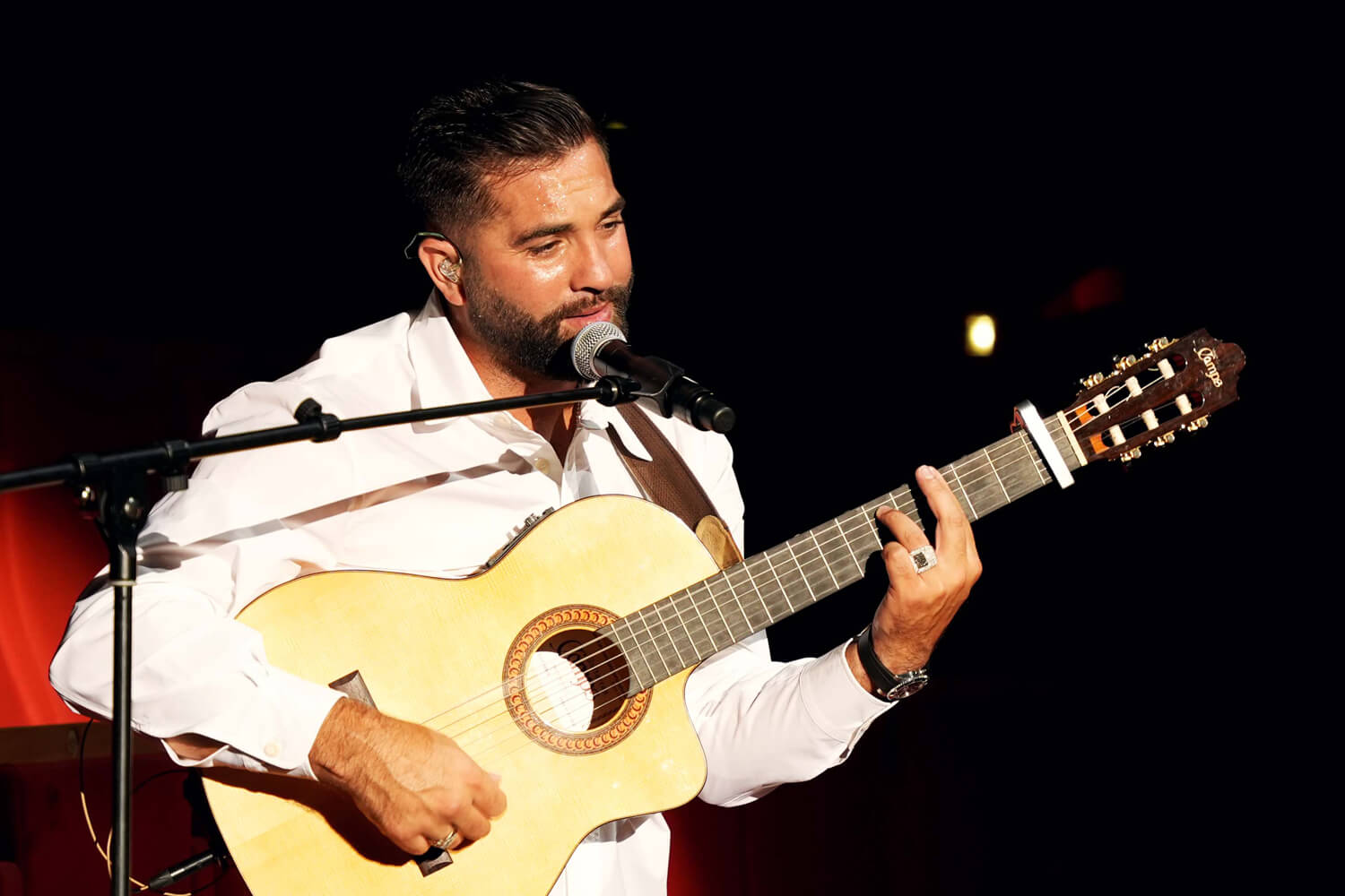 Kendji Girac à la guitare lors d'un concert à la Salle 3000 de Lyon Kendji Girac en plan rapproché, chantant au microphone et jouant de la guitare sur fond sombre