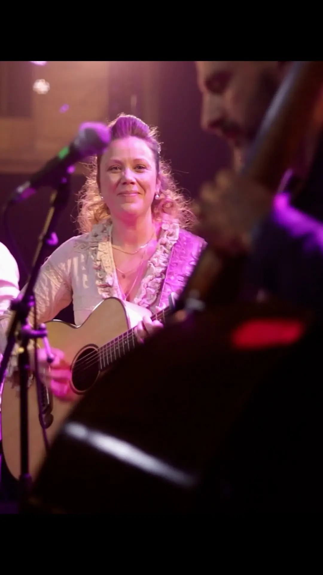 Une guitariste de Silène & the Dreamcatchers sur scène sous un éclairage violet, avec un musicien flou au premier plan.